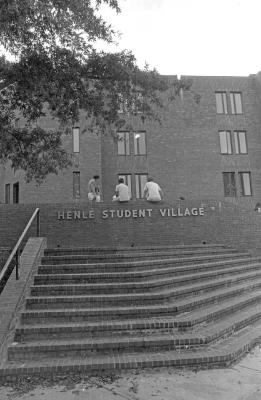 Black and white image of Henle Village in 1978 showing three students sitting on the wall with the complex's name at the top of the Henle stairs.