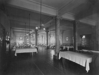 Black and white image of Ryan's dining room in 1906 showing large banquet tables set with white table cloths among the room's floor to ceiling pillars.