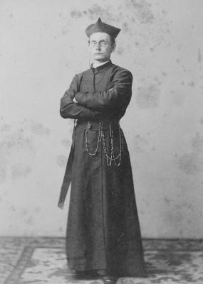 Black and white image of Fr. Joseph Havens Richards depicting him standing tall with arms crossed and dressed in his clerical robes and biretta. 