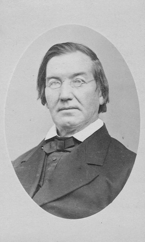 Black and white headshot of Fr. John Early, S.J. showing him in formal attire with his glasses perched upon his nose.